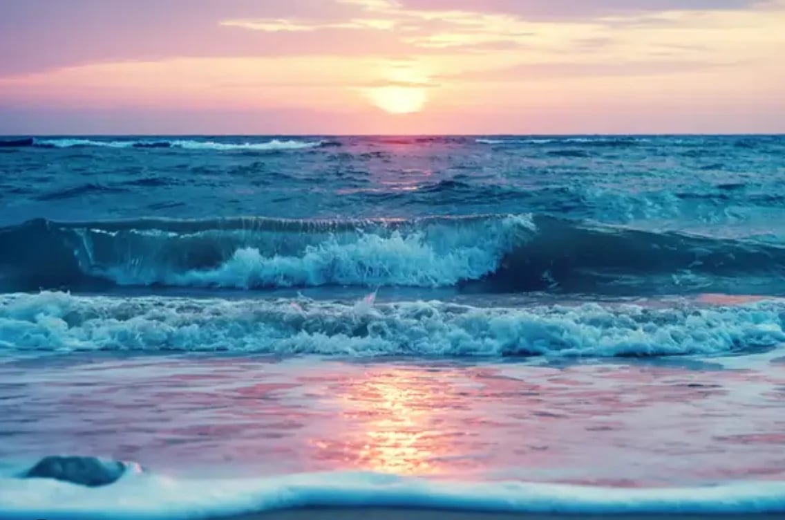 Ocean waves crashing on beach at sunset with pink and gold sky reflected on water